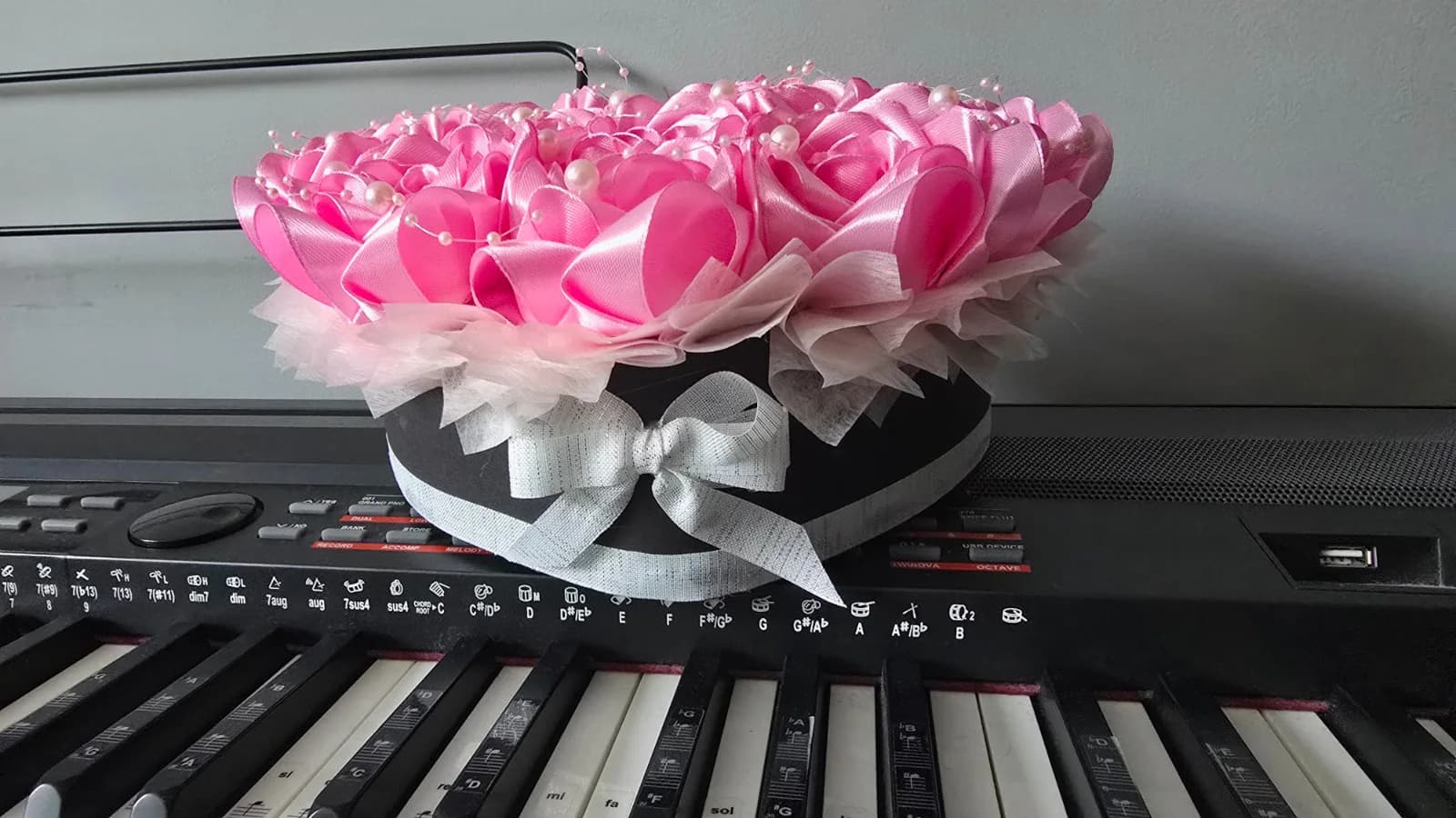 Różowy flower box z czarną podstawą i jasną kokardą widziany z boku